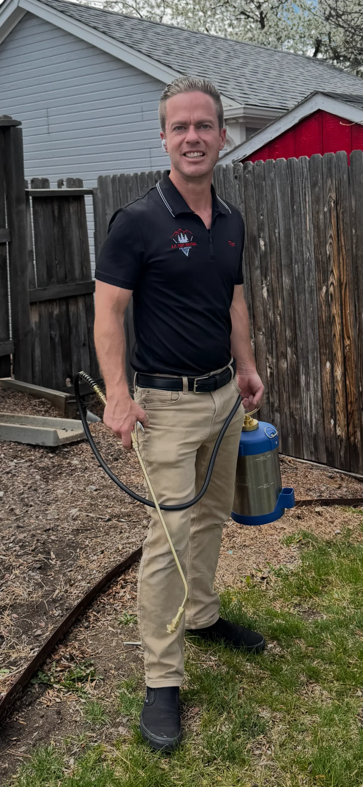 A technician stands in a residential backyard, ready to perform a targeted pest treatment along a fence line